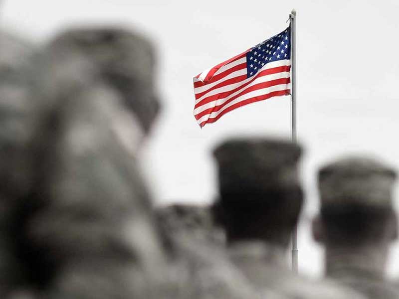 Military standing in front of an American flag and saluting it