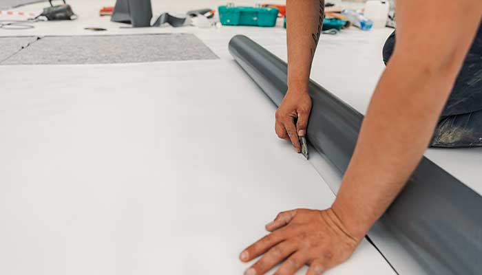 Close up of worker cutting a sheet of TPO for a commercial roof project